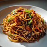 A close-up of a mound of glossy, savory fried noodles mixed with sliced mushrooms, carrots, and green onions.