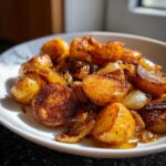 Close-up of golden brown, crispy fried potatoes mixed with caramelized onions served on a white plate.