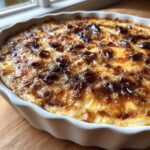 Close-up of a freshly baked caramelized onion dip with a golden-brown, bubbly top layer of cheese and dark caramelized onions.