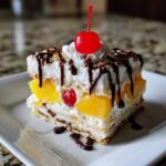 A delicious slice of banana split cake layered with whipped cream, pineapple, and topped with chocolate syrup and a maraschino cherry.