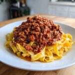 A generous serving of rich, meaty bolognese sauce piled high on fresh tagliatelle pasta on a white plate.