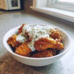 Crispy buffalo wings generously topped with creamy blue cheese dip and sprinkled with herbs.