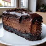 A rich, dark slice of chocolate cheesecake topped with dripping chocolate ganache and crumbs.