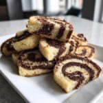 A stack of freshly baked pinwheel cookies showing a clear chocolate swirl pattern on a white plate.