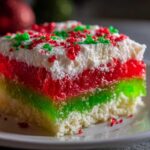 Close-up of a slice of Christmas poke cake featuring white cake, vibrant red and green jello layers, and whipped topping with sprinkles.