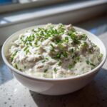A white bowl filled with creamy clam dip, generously topped with freshly chopped green chives.