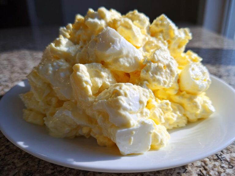 A close-up of a generous mound of creamy, yellow and white egg salad recipe served on a white plate.