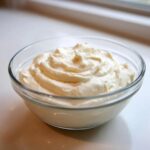 A clear glass bowl filled with freshly whipped, thick creamy horseradish sauce.