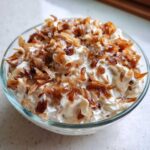 Close-up of a creamy onion dip served in a clear glass bowl, generously topped with crispy, caramelized fried onions.
