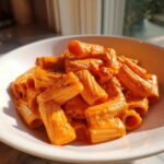 A close-up shot of rigatoni pasta coated generously in vibrant pink sauce pasta, served in a white bowl.