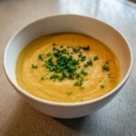 A creamy bowl of yellow roasted cauliflower soup garnished with fresh chopped chives and black pepper.