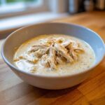 A close-up of a bowl filled with creamy white chicken chili, topped generously with shredded chicken.