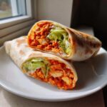 A crispy buffalo chicken wrap sliced in half, revealing spicy chicken, lettuce, and creamy sauce.