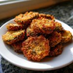 A close-up of a pile of perfectly golden, crispy Fried Pickles served on a small white plate.