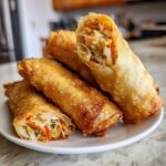 A stack of golden brown, crispy homemade egg roll appetizers, one cut open to show the vegetable filling.