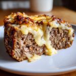 Close-up of a juicy slice of crockpot french onion meatloaf topped with melted, gooey cheese.