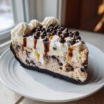 A rich slice of chocolate chip ice cream pie with whipped cream, caramel drizzle, and mini chocolate chips.