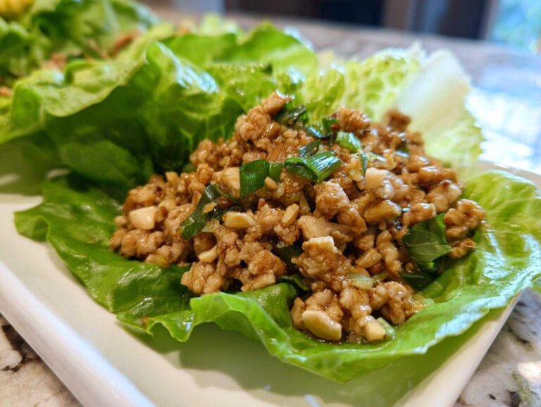 Close-up of savory chicken lettuce wraps filling served in a crisp butter lettuce cup, garnished with green onions.
