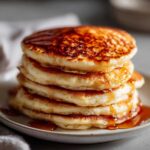 Close-up of a tall stack of fluffy almond flour pancakes drizzled generously with golden syrup.