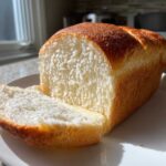 Close-up of a freshly baked loaf of japanese milk bread, showing its incredibly soft, white interior and golden crust.