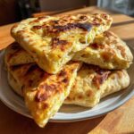 A stack of golden-brown, fluffy pieces of homemade naan bread recipe, showing a soft interior.