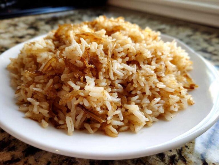 A close-up of fluffy french onion butter rice served on a white plate, showing caramelized onions mixed throughout the grains.