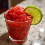 Close-up of a vibrant red, icy strawberry daiquiri garnished with a bright green lime wheel.