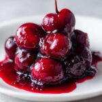 Close-up of glossy, whole cherries coated in thick, rich sauce, perfect for cherry pie filling.
