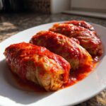 Three hearty cabbage rolls smothered in bright red tomato sauce served on a white platter.