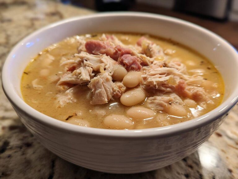 Close-up of a white bowl filled with rich navy bean soup topped with shredded chicken and ham pieces.
