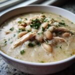 Close-up of a hearty bowl of instant pot white chicken chili topped with shredded chicken, white beans, and fresh parsley.