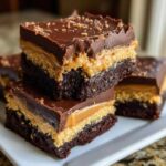 Two stacked squares of rich, three-layer buckeye brownies featuring a dark chocolate base, peanut butter filling, and chocolate ganache topping.