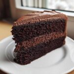 Close-up of a rich, moist slice of chocolate cake recipe layered with dark chocolate frosting on a white plate.
