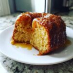 A close-up of a moist, golden slice cut from a bundt rum cake recipe, dripping with a rich glaze.