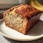 A freshly baked loaf of moist sourdough banana bread with a golden-brown crust, sitting on a plate.