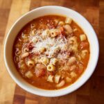 Overhead view of a steaming bowl of pasta fagioli, rich with beans, pasta, and topped with grated Parmesan cheese.
