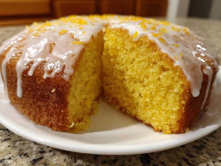 A slice cut from a round orange juice cake topped with white glaze and orange zest.