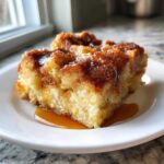 A close-up of a square serving of moist overnight french toast topped with caramelized cinnamon sugar and drizzled with syrup.