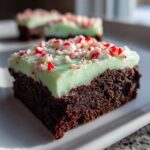 A decadent square of peppermint brownies featuring a rich chocolate base, light green mint frosting, and crushed candy canes.