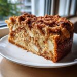A generous slice of homemade apple crumb cake showing chunks of apple and a thick cinnamon streusel topping.