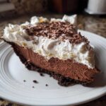 A decadent slice of french silk pie featuring a chocolate crust, creamy chocolate filling, and thick whipped cream topped with chocolate shavings.