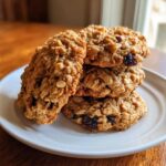 A stack of four soft, chewy oatmeal raisin cookies piled on a white plate, showing visible oats and raisins.