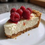A perfect slice of white chocolate mousse tart with a graham cracker crust, topped with fresh raspberries and raspberry drizzle.