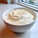 Close-up of a thick, creamy white garlic sauce swirled in a bowl, topped with fine minced garlic.