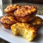 A stack of golden brown, fluffy 12-egg bites, with one bite taken out showing the cheesy interior.