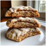 Three stacked cinnamon roll cookies, cut in half to show the soft, swirled interior and thick vanilla glaze.
