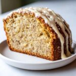 Close-up of a moist slice of eggnog bread topped with a thick, dripping vanilla glaze and nutmeg sprinkles.