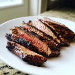 Slices of juicy, grilled flank steak cooked medium-rare, seasoned with herbs, served on a white plate.