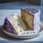 Two slices of amazing lavender cake with light purple frosting and dried lavender topping on a white plate.