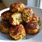 A pile of perfectly browned stuffing balls, one is broken open showing the fluffy interior.